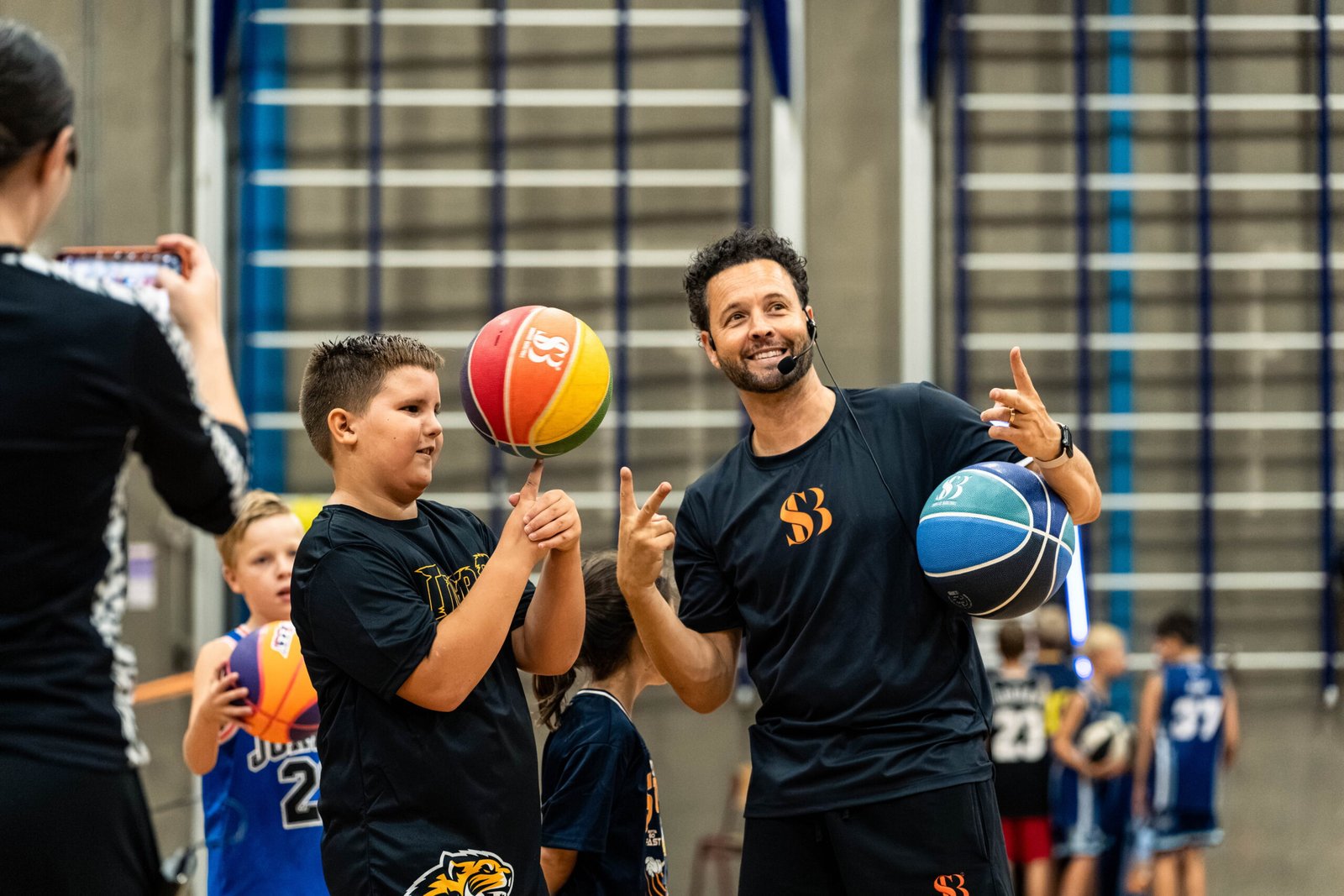 Jonge deelnemer laat de bal op zijn vinger draaien naast Galdino tijdens het jubileum van BV Alphia