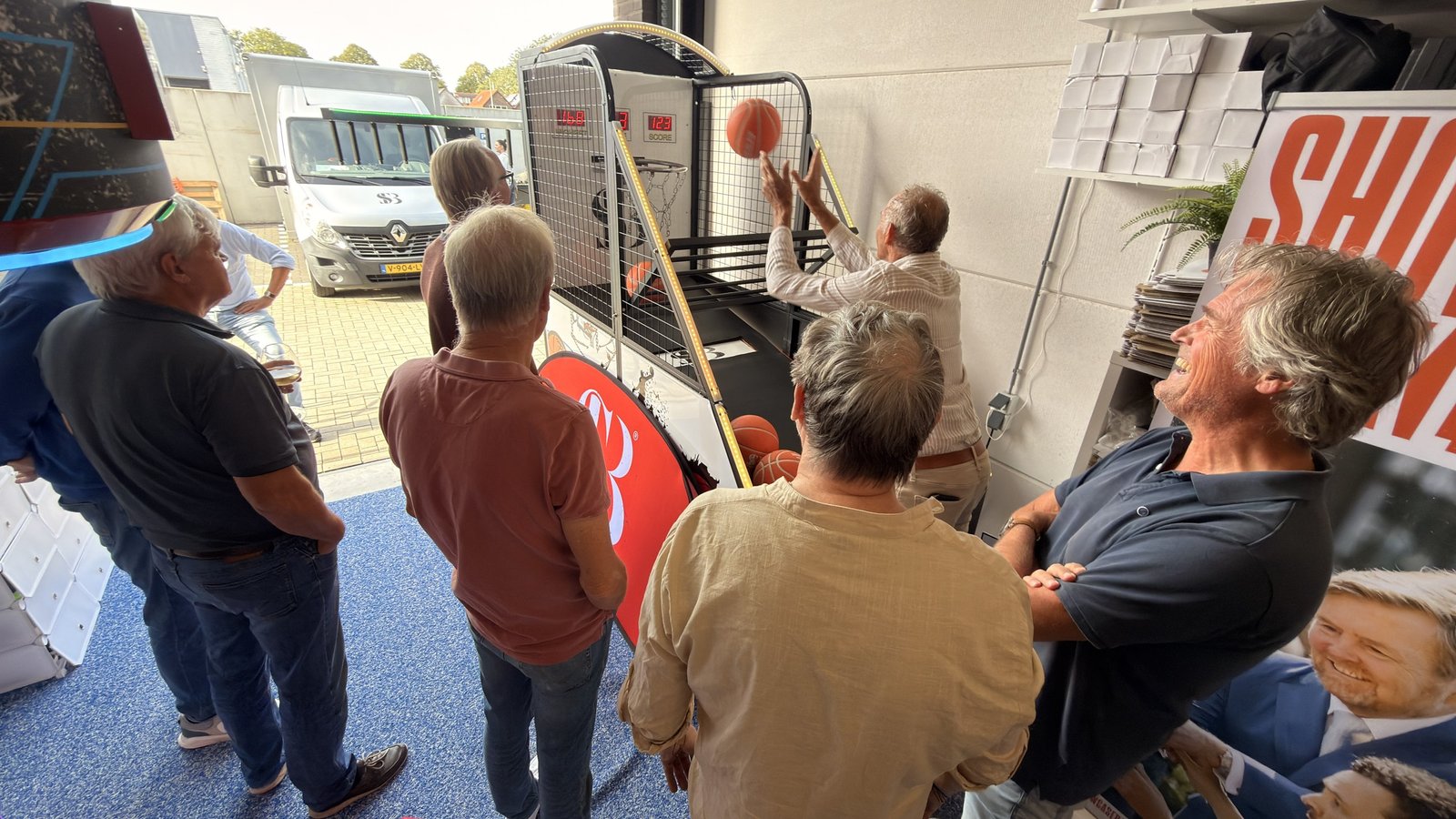 Gasten kijken mee terwijl een van de heren scoort op de basketbal arcade machine